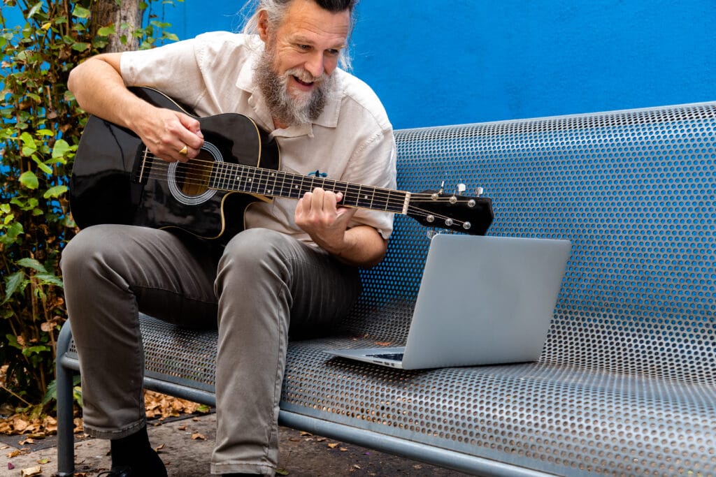 Homem de meia idade, com barba grande e grisalha, com um anel na mão direita, tocando um violão na cor preta